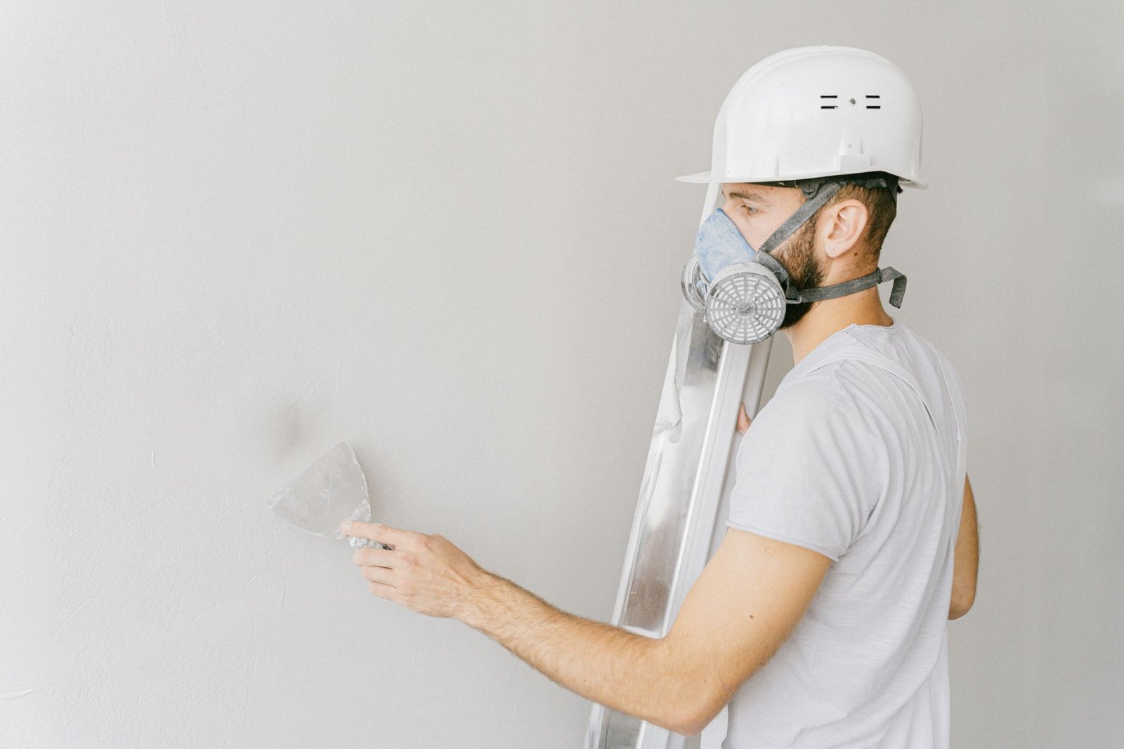 Handwerker mit Atemschutzmaske und Schutzhelm bei Sanierungsarbeiten an einer Wand – Schutzausrüstung bei Asbestsanierung im Gewerbegebäude