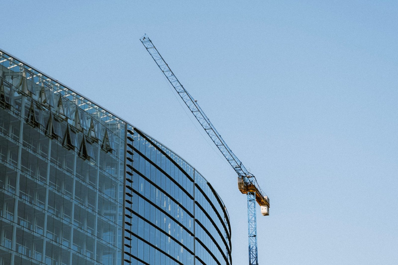 Modernes Gewerbegebäude mit Glasfassade im Bau, daneben ein Baukran vor blauem Himmel – symbolisiert CSRD-Anforderungen an Gewerbeimmobilien-Bauprojekte