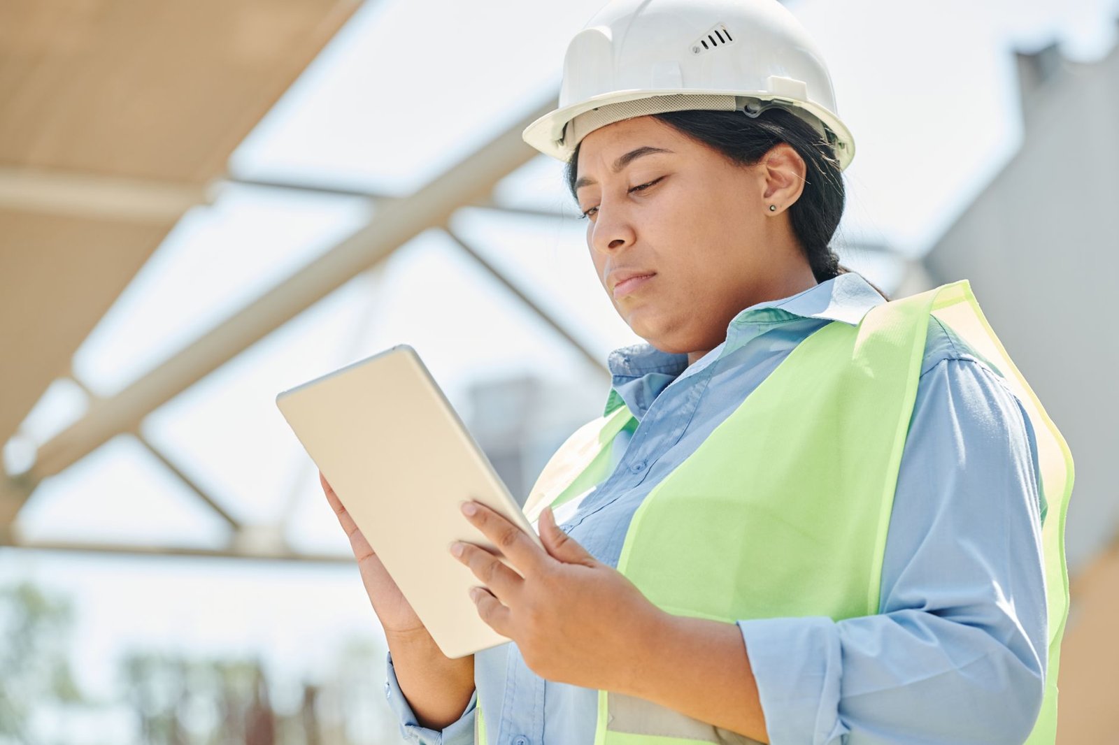 Baustellenmitarbeiterin mit Schutzhelm und Warnweste liest auf einem Tablet – symbolisiert digitale Dokumentation auf Bauprojekten