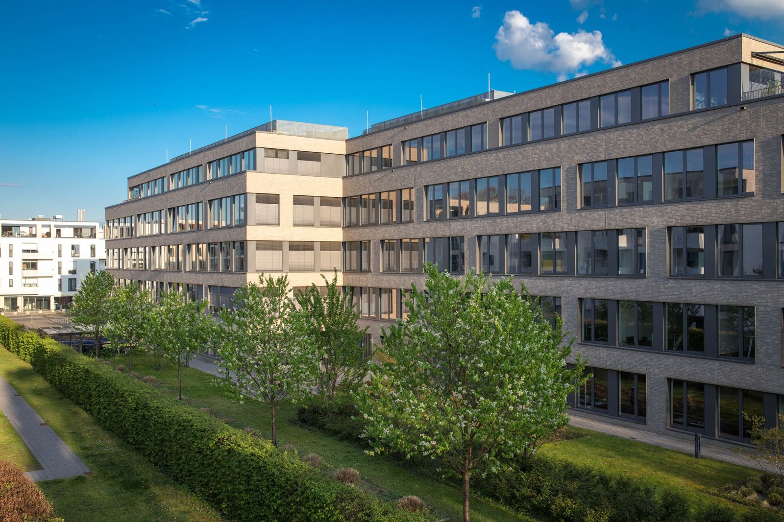 Modernes Büro- und Gewerbegebäude aus Backstein mit großen Glasfronten, umgeben von grüner Bepflanzung und Bäumen unter blauem Himmel – symbolisch für nachhaltige Gewerbeimmobilien im Kontext der EU-Taxonomie