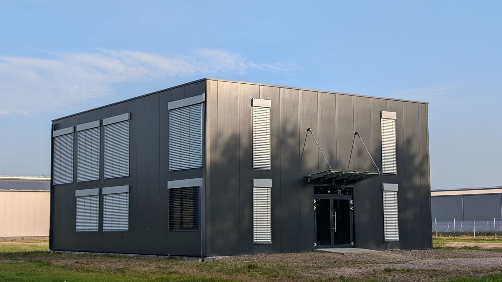 Zweigeschossiges Gewerbegebäude in modularer Stahlbauweise mit seriellen Fassadenelementen und Rollläden, freistehend auf Gewerbegelände