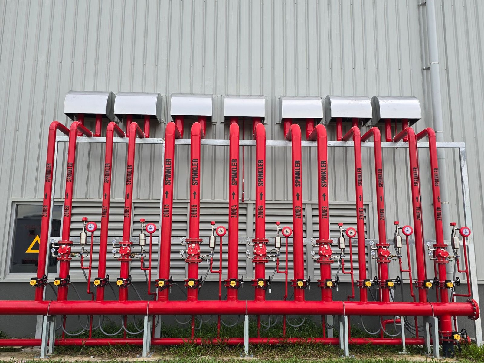 Rote Steuerventilstation einer industriellen Sprinkleranlage an der Außenwand eines Industriegebäudes – Brandschutz in Logistikhallen